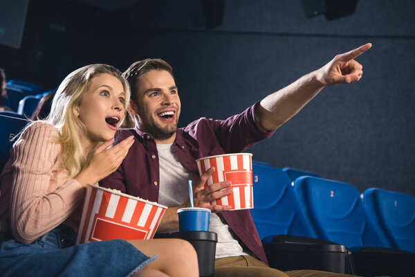 shocked couple with popcorn and soda drink watching film together in cinema