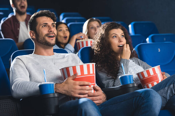 emotional couple with popcorn watching movie together in cinema 