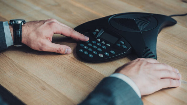 обрезанный снимок бизнесмена с помощью конференц-телефона на рабочем месте
