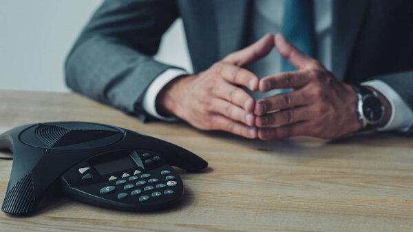 cropped shot of businessman sitting in front of speakerphone and having conversation at office