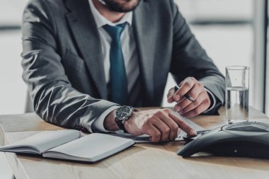 yakışıklı işadamı ofisinde masada konferans telefon kullanarak kırpılmış atış