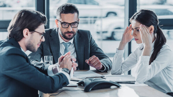 серьезные деловые люди, беседующие и пользующиеся громкой связью в современном офисе
