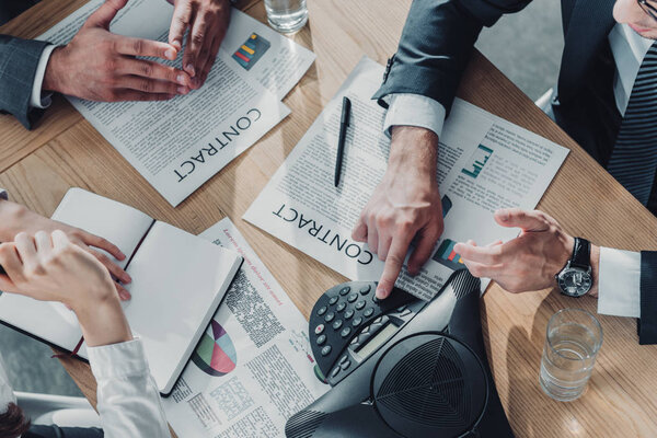 обрезанный снимок деловых людей, беседующих с контрактами и громкоговорителем на столе в современном офисе
