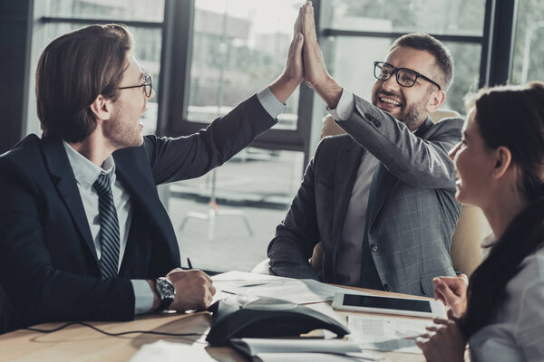 счастливые бизнесмены дают высокую пятерку во время встречи в современном офисе

