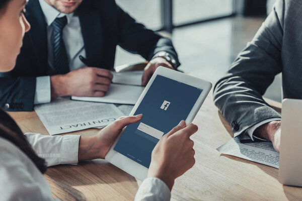 обрезанный снимок предпринимательницы, держащей планшет с приложением facebook на экране во время встречи
