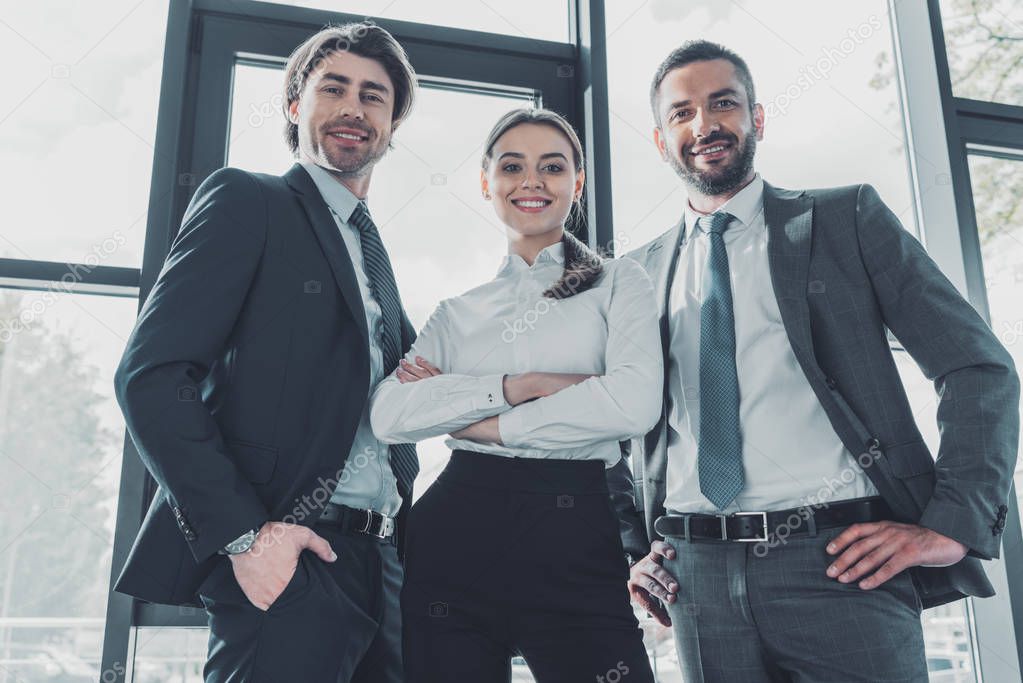 bottom view of group of smiling young business people standing at modern office and looking at camera