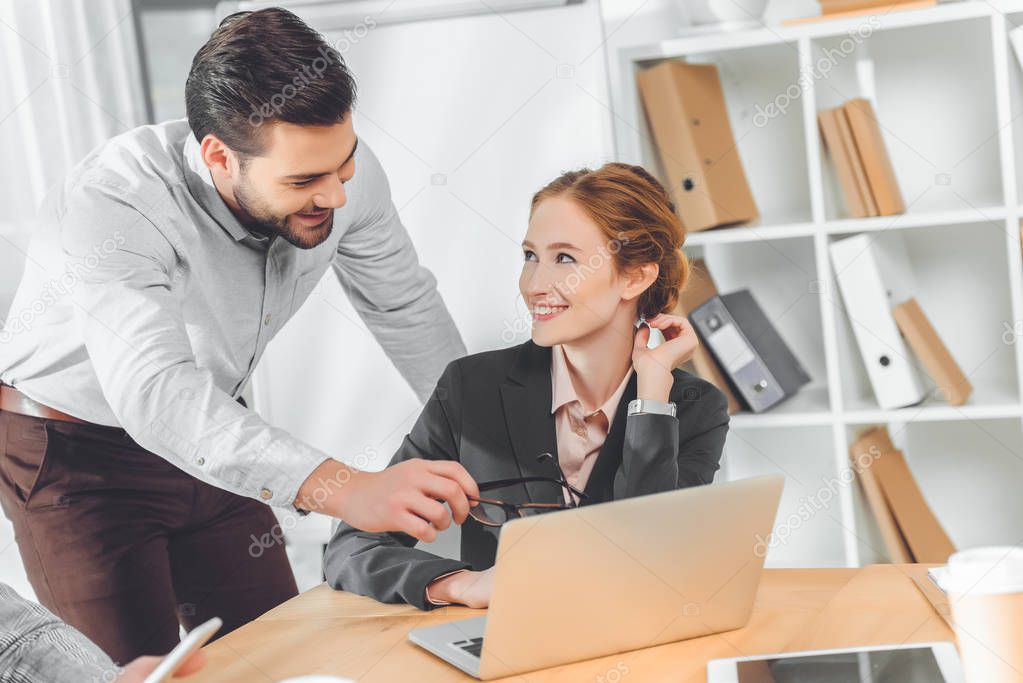 standing man in blue shirt speaking to sitting woman against laptop on table 