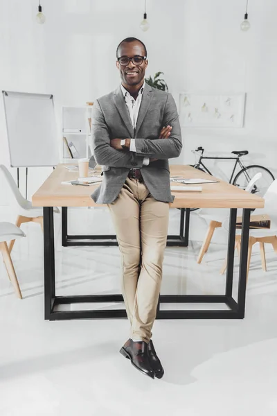 Усміхнений Африканський Чоловік Спирається Стіл Обіймами Схрещеними Офісному Просторі — стокове фото