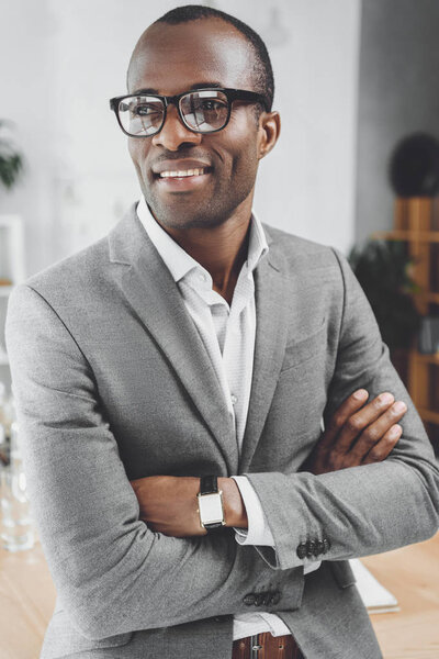 smiling african man with arms crossed looking away at office space 
