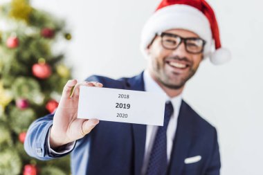 Noel Baba şapkası 2019 kartıyla ofiste holding içinde gülümseyen iş adamı