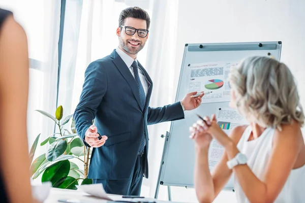 オフィスでのプレゼンテーション中にフリップチャートに指しているビジネスマンを笑顔 — ストック写真
