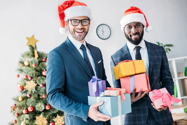 Sonrientes Hombres Negocios Multiculturales Sombreros Santa Celebración Cajas Regalo Oficina — Foto de Stock