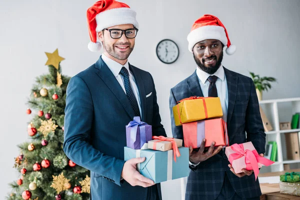 Sonrientes Hombres Negocios Multiculturales Sombreros Santa Celebración Cajas Regalo Oficina — Foto de Stock