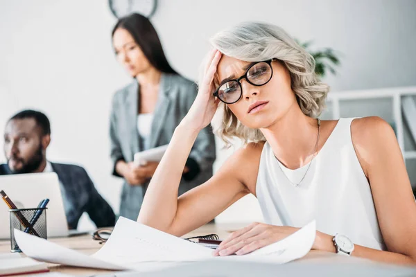 Exhausted caucasian businesswoman sitting at table in office and looking at documents — Stock Image Exhausted Caucasian Businesswoman Sitting Table Office Looking Documents Royalty Free Stock Images