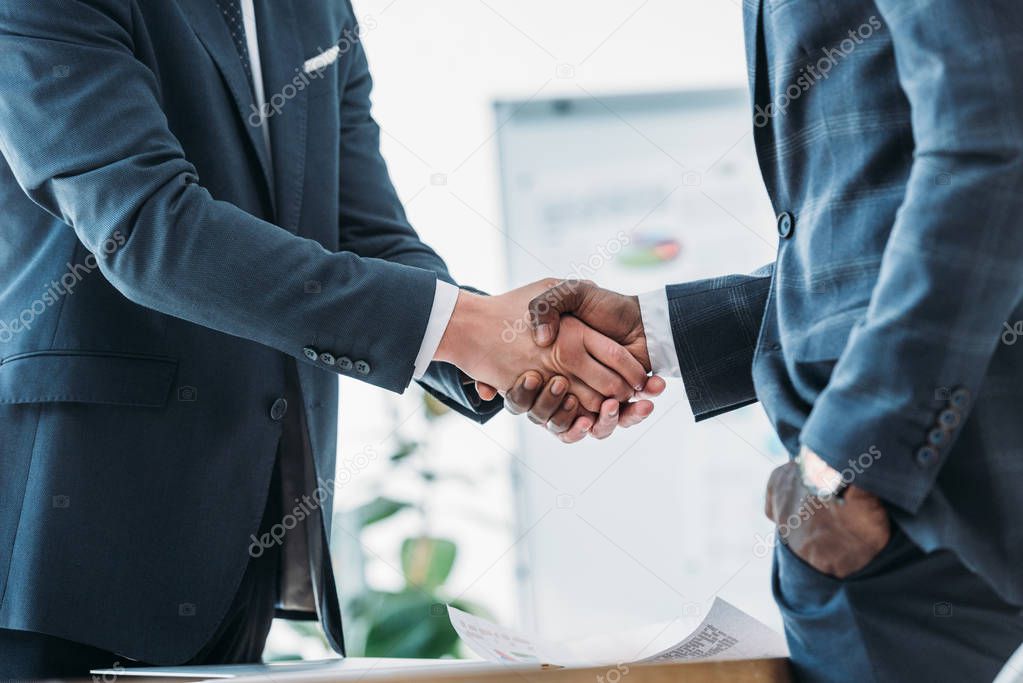 cropped image of multicultural businessmen in suits shaking hands in office