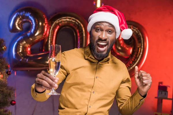 新年企業パーティーでシャンパン グラスを持ってサンタ帽子のアフリカ系アメリカ人のビジネスマンを興奮 — ストック写真