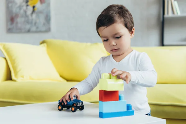 コンス トラクター ブロックと自宅のテーブルの上のおもちゃの車で遊ぶ少年 — ストック写真