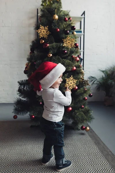 Cute Smiling Boy Santa Hat Pointing Christmas Tree — Free Stock Photo