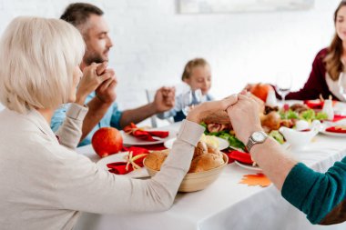 family holding hands and praying together before thanksgiving dinner at served table with turkey  clipart