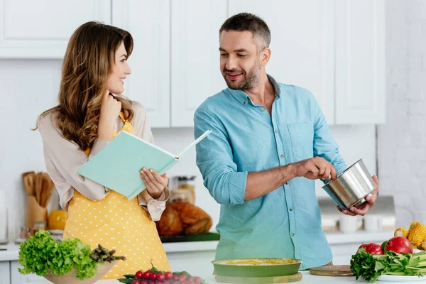 Smiling Couple Reading Recipe Book While Cooking Together Kitchen — Stock Photo, Image