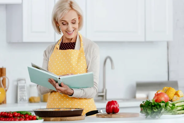 Donna Anziana Sorridente Che Legge Libro Ricette Mentre Cucina Cucina — Foto Stock