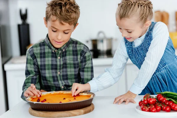 cute siblings decorating thanksgiving pumpking pie with berries together at kitchen