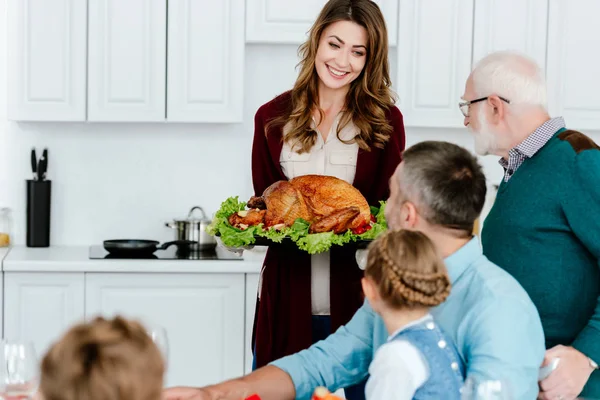 家族で感謝祭のディナーのために焼きたてのトルコを運ぶ笑顔の女性 — ストック写真