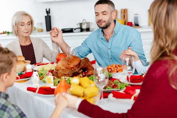 happy family praying at served table with turkey before holiday dinner on thanksgiving