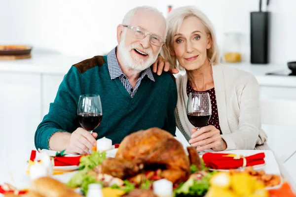 portrait of happy senior couple with wine glasses at served table with delicious turkey on thanksgiving