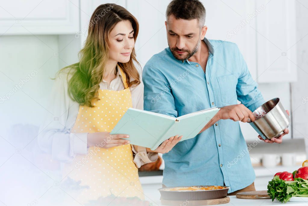 beautiful couple reading recipe book while cooking together at kitchen