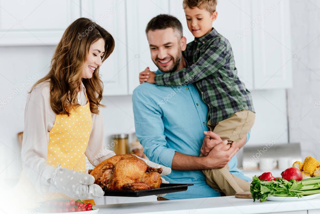 happy little kid with parents preparing thanksgiving turkey together at kitchen