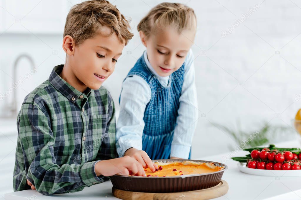 adorable siblings decorating pumpking pie with berries together at kitchen