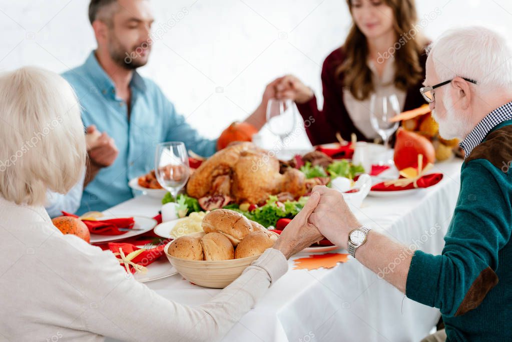 selective focus of family praying at served table with turkey before holiday dinner on thanksgiving 