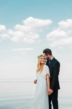 Evlilik çift elele ve birbirine kumsalda bakarak takım elbise ve beyaz elbise