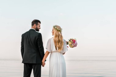 Arkadan Görünüş kumsalda ayakta, el ele tutuşarak ve birbirine bakarak düğün çift