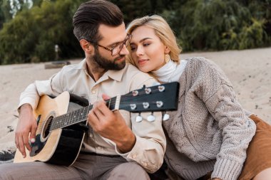 yakışıklı erkek sonbahar kıyafeti kumsalda çekici kız için akustik gitar çalmak