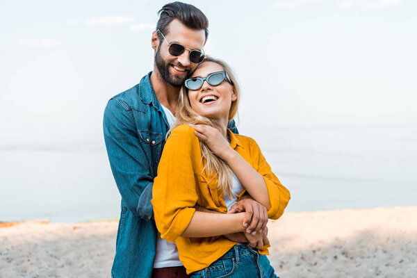 парень обнимает смеющуюся девушку на пляже
