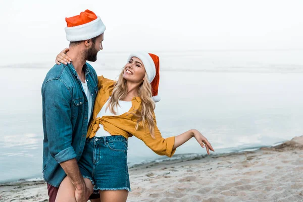 Ζευγάρι Καπέλα Santa Αγκάλιασμα Και Έχοντας Διασκέδαση Στην Παραλία — Φωτογραφία Αρχείου