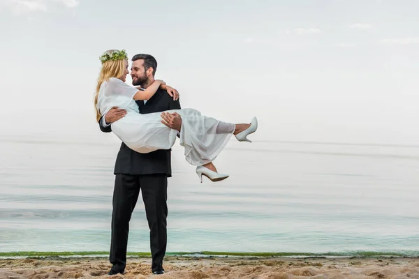 Noivo Bonito Terno Segurando Noiva Atraente Vestido Branco Praia — Fotografia de Stock