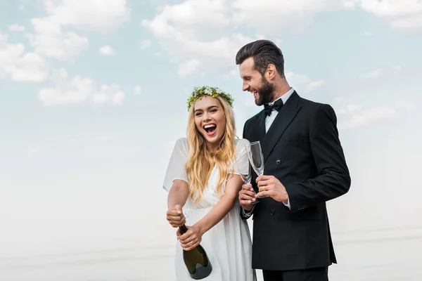 Счастливая Невеста Белом Платье Открывает Бутылку Шампанского Пляже — стоковое фото