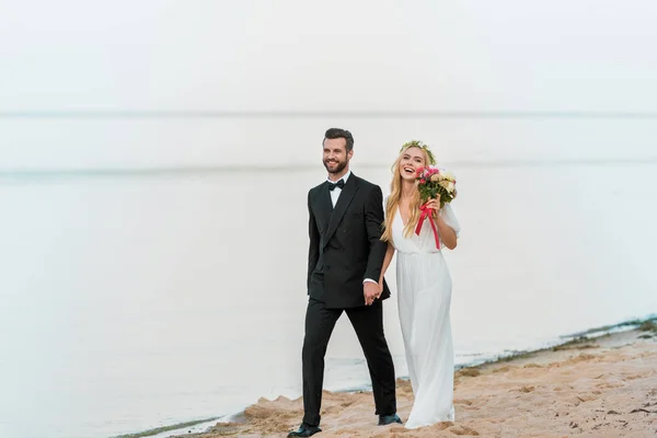 Leende Bröllopsparet Håller Hand Och Promenader Stranden — Stockfoto