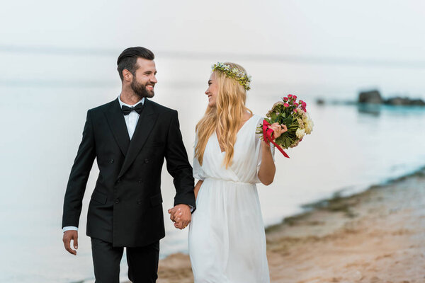 affectionate wedding couple holding hands, walking and looking at each other on beach