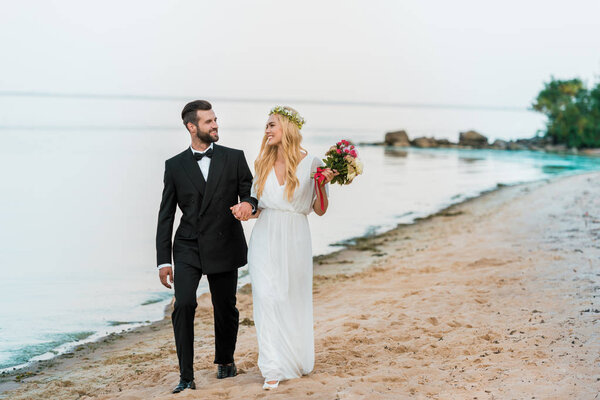 wedding couple holding hands and walking on sandy ocean beach