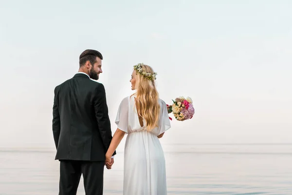 Vista Posteriore Coppia Nozze Piedi Sulla Spiaggia Tenendosi Mano Guardandosi — Foto Stock