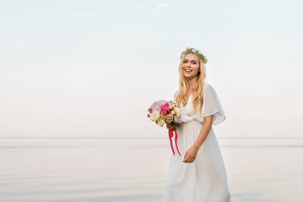 Улыбающаяся Привлекательная Невеста Белом Платье Венке Свадебным Букетом Прогулкой Моря — стоковое фото