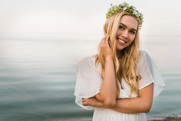 美丽的新娘在白色礼服和花花圈看在海滩的照相机 — 图库照片