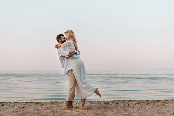 bride in white dress and groom cuddling on beach
