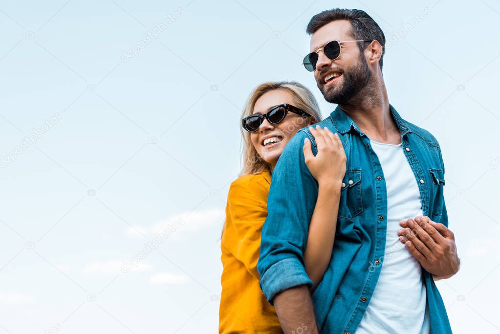 low angle view of smiling girlfriend hugging boyfriend against blue sky