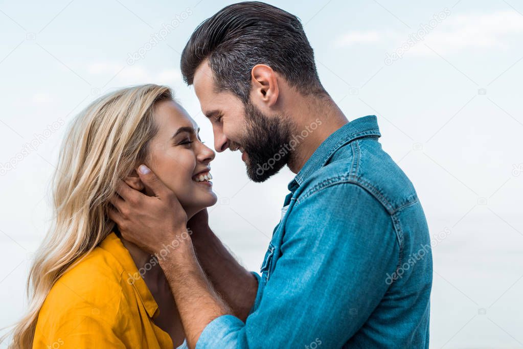 side view of smiling couple hugging and going to kiss against blue sky