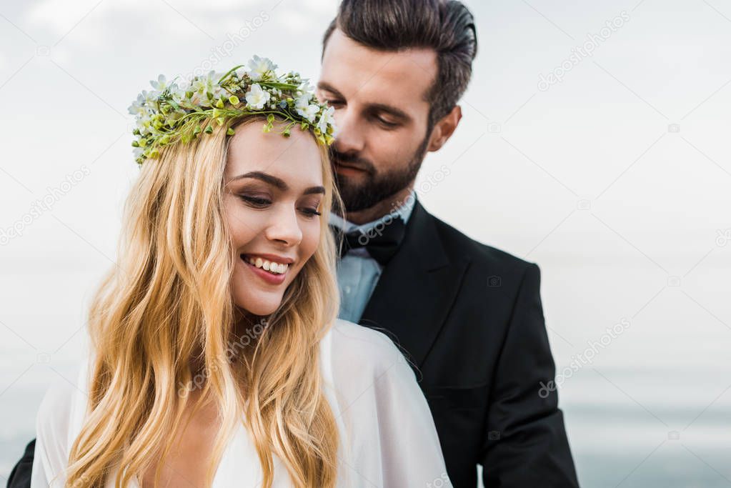 portrait of handsome groom in suit hugging attractive bride on beach